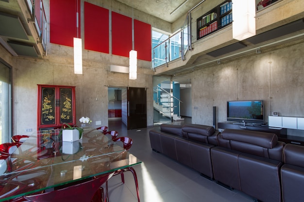 Interieur van modern huis, eetkamer met glazen tafel en rode methacrylaat stoelen, dubbele hoogte.