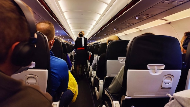 Interieur van vliegtuig met passagiers op stoelen en stewardess in uniform door het gangpad