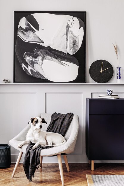 Interieur van woonkamer met stijlvolle fauteuil geruite zwarte klok cactussen marmeren kruk moderne schilderijen decoratie en mooie hond liggend op de fauteuil