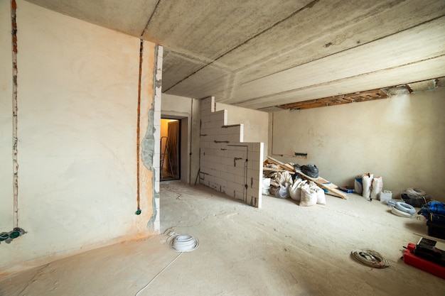 Interior of an apartment room with bare walls and ceiling under construction.
