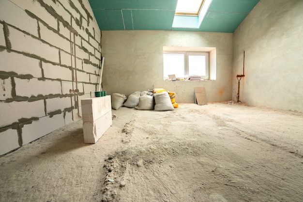 Interior of an apartment room with bare walls and ceiling under construction.