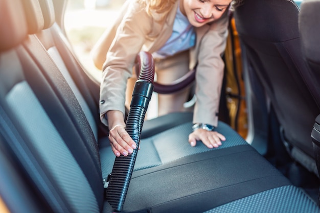 Dettagli interni dell'auto. felice imprenditrice pulisce l'interno della sua auto con l'aspirapolvere.