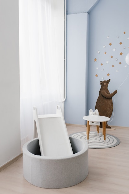 Photo the interior of the children's room is decorated in blue and beige colors. the bear holds a small balloon in his hands. slide with a pool made of plastic balls