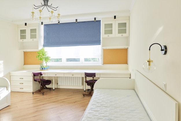 Interior of children's room for two children in light colors. White furniture, table, knee orthopedic chairs, blue roman blind on the window