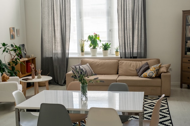 Interior of comfortable domestic room in a flat or house with table in the center surrounded by chairs, couch with cushions and armchair