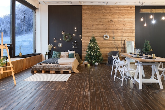 Интерьер загородного дома украшает новогодняя елка. большой просторный светлый номер, отделанный деревом, с простой деревянной мебелью