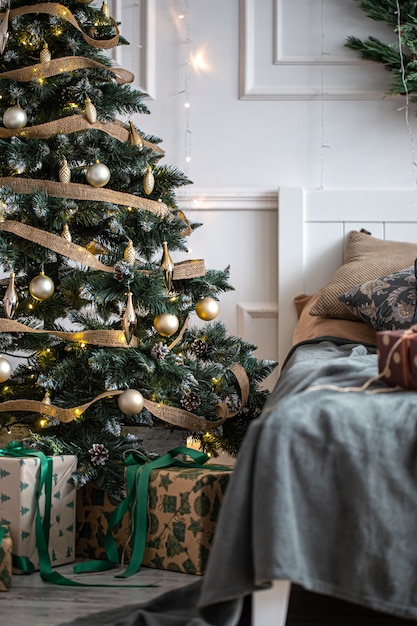 クリスマスツリーとベッドの上のギフトボックスのある居心地の良い部屋のインテリア、装飾のためのデザインのアイデア。