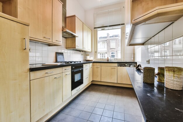 Interior of cozy simple kitchen with light wooden cabinets and black appliances in daylight