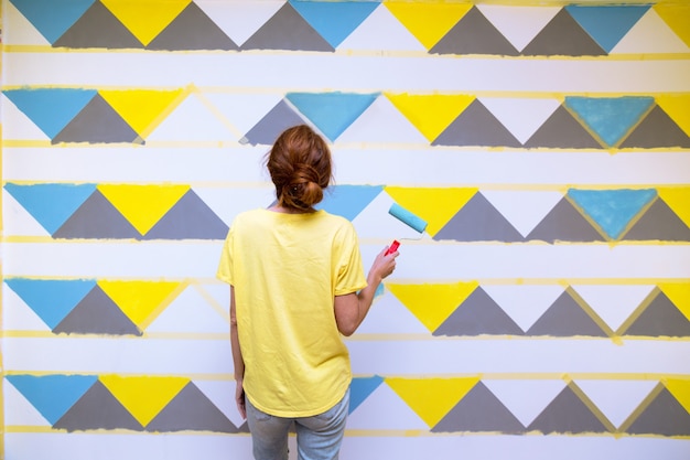 Foto interior design. la ragazza dipinge il muro in un motivo geometrico.