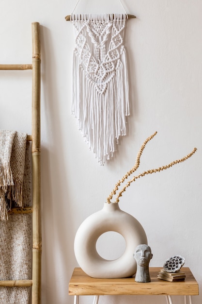 Interior design of living room with stylish dried flowers in vase, wooden ladder, plaid, white macrame and personal accessories in home decor.