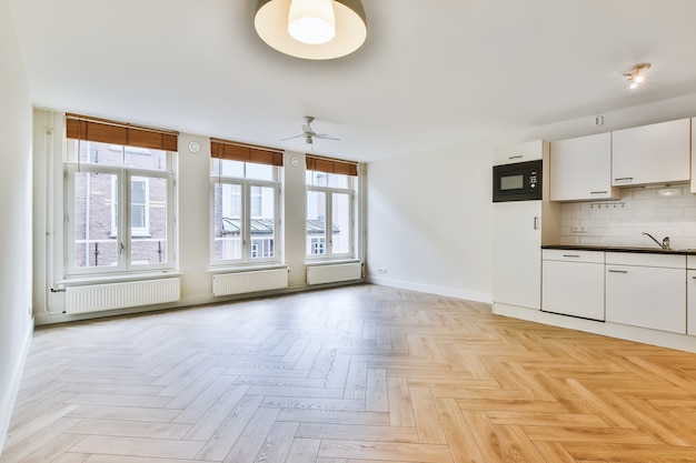 Interior design of spacious empty studio apartment with large windows and laminate floor and white walls furnished with kitchen set