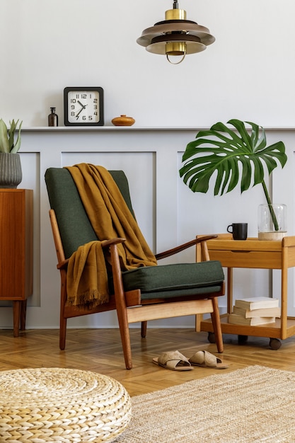 Interior design of stylish living room with vintage green armchair, coffee table, furniture, grey wall, shelf, carpet, plants, leaf in vase, pouf, pendant lamp and elegant personal accessories.