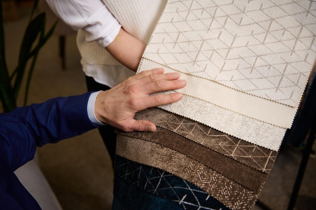 Interior designer points to the fabric that he likes choosing\
the fabric in the catalog with fabric samples for new sofa