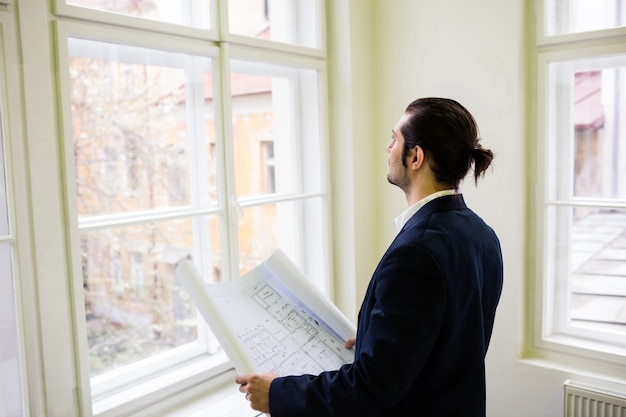 Interior designer with blueprint looking though window