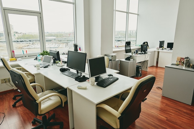 Интерьер пустого современного офиса с настольными компьютерами на столах, расположенных рядом друг с другом
