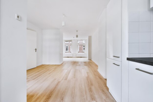 Interior of an empty room next to the kitchen room with white walls and large windows