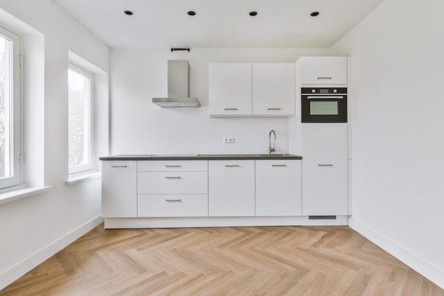 Interior of empty white kitchen with windows and wooden parquet floor