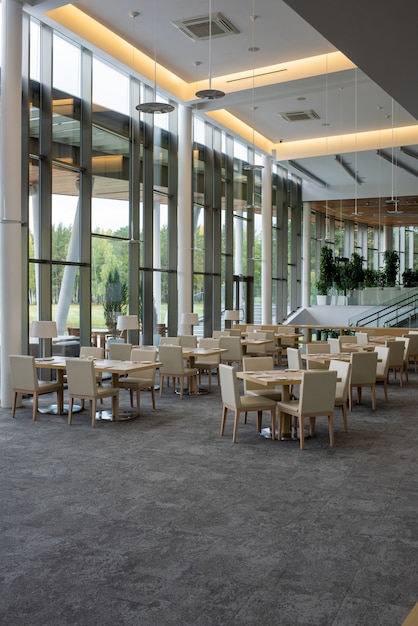 Photo interior of five star restaurant inside contemporary business center with many tables surrounded by chairs standing along big windows