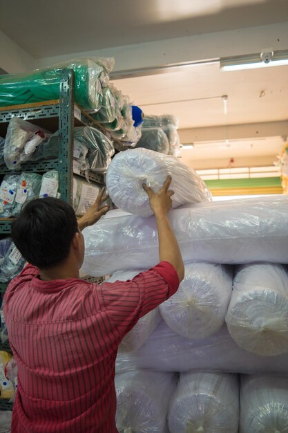 Interior of a industrial warehouse with many shelves with colorful fabric rolls on them The worker lift the roll fabric and check quantity