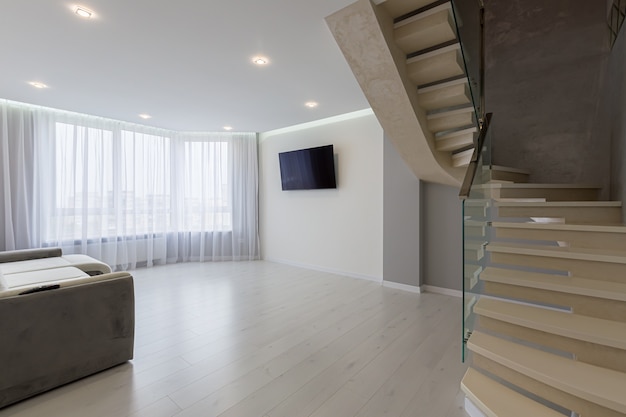 Интерьер большой гостиной с серыми стенами и лестницей в современном стиле