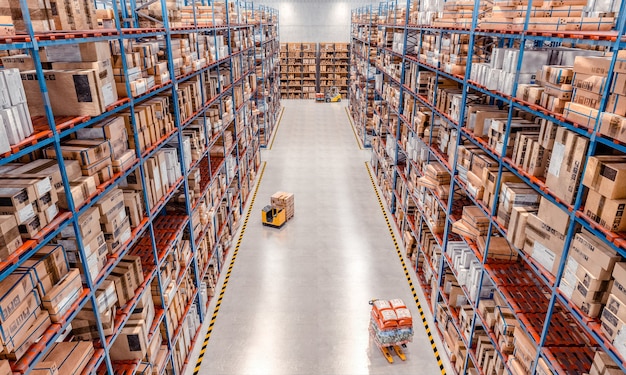 Interior of a large warehouse with very high shelves and lifting equipment in action