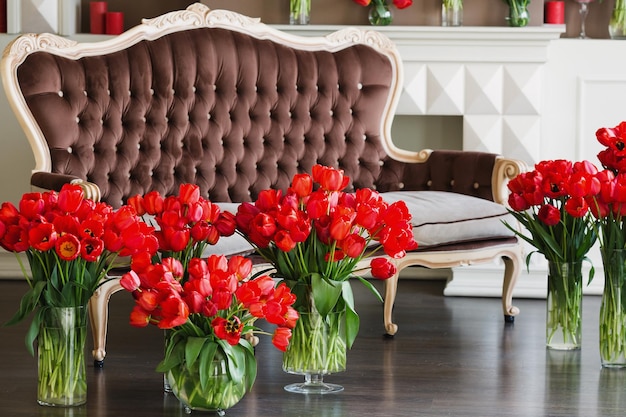 The interior of the living room in brown tones with large bouquets of red tulips in vases.