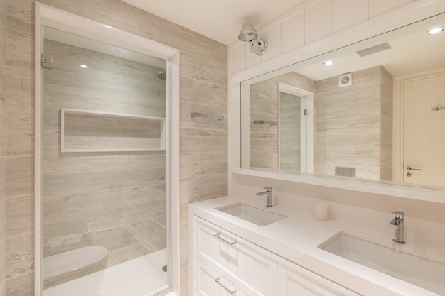 Interior of modern bathroom. Transparent door to the shower and two sinks in refurbished apartment