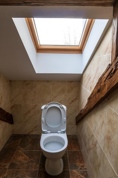 The interior of a modern bathroom with decorative elements made of wood A large window over the toilet A low ceiling with a window in the restaurant toilet