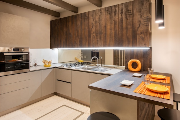 Interno della moderna cucina attrezzata con accenti arancioni e armadi di colore beige neutro con illuminazione ad incasso