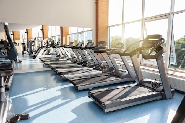 Interno della moderna sala fitness della palestra con grandi finestre e tapis roulant