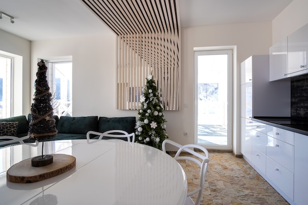 Интерьер современной просторной кухни с белыми стенами, декоративными деревянными элементами, современной мебелью и большим мягким диваном.