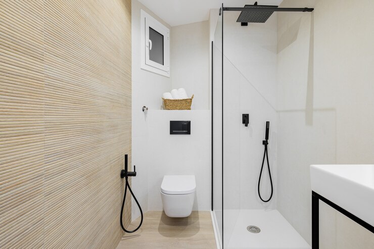 Interior of modern style bathroom in white and beige colors in refurbished apartment shower zone and toilet with black faucets towels and tiled floor and walls