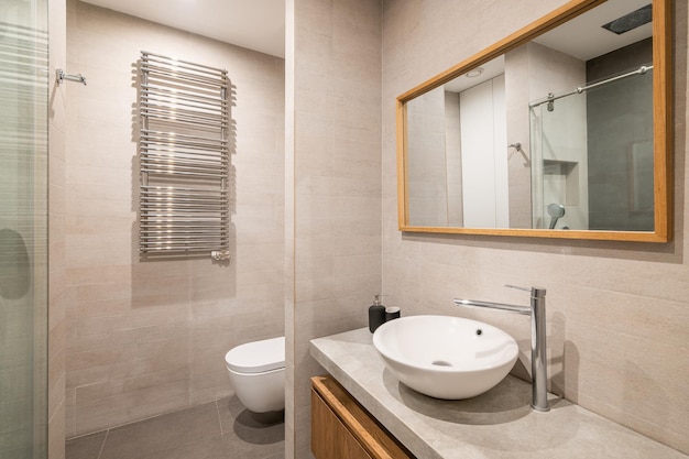 Interior of modern tiled bathroom with white toilet radiator and shower in reflection of wooden