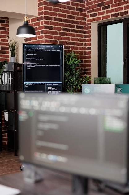 プログラミングラインコードを表示する複数のコンピュータ画面を備えた空のデータセンターオフィスの内部。モダンなレンガの壁のインテリアと高品質のハードウェアとソフトウェアテクノロジーを備えたサーバールーム。