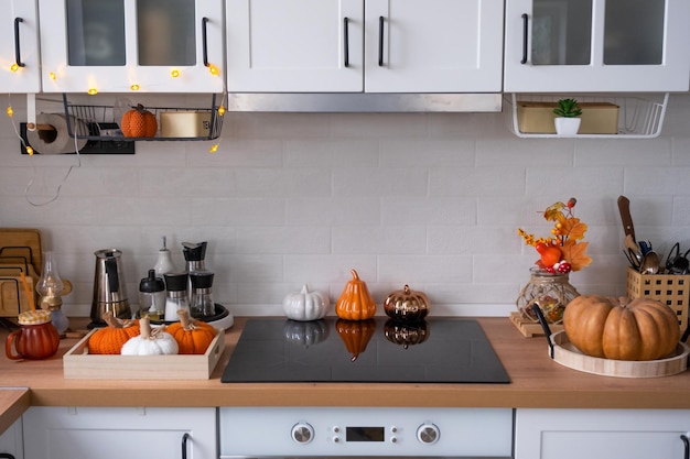 スカンジスタイルの白いキッチンのインテリアは、ハロウィーンのカボチャで飾られています 休日の秋の気分の家の装飾