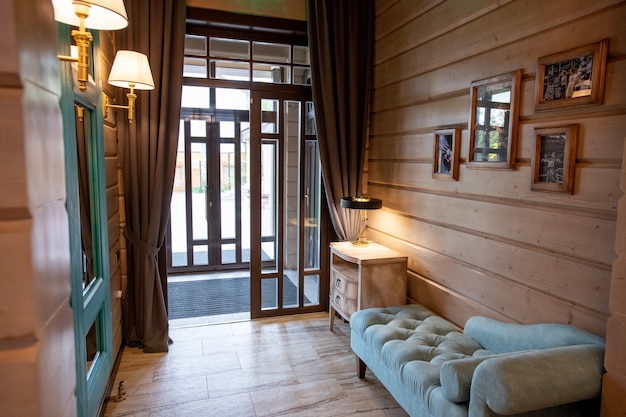 Interno della piccola camera confortevole con divano in morbido velluto e comodino con lampada lungo la parete in legno dalla porta aperta