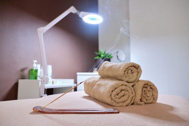 Interior of spa cabinet, massage table, towels, cosmetics, massage oils, aroma sticks with smoke