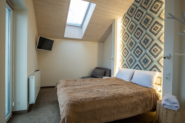 Interior of a spacious hotel bedroom on attic floor with fresh linen on a big double bed. Cozy contemporary mansard room in a modern house.