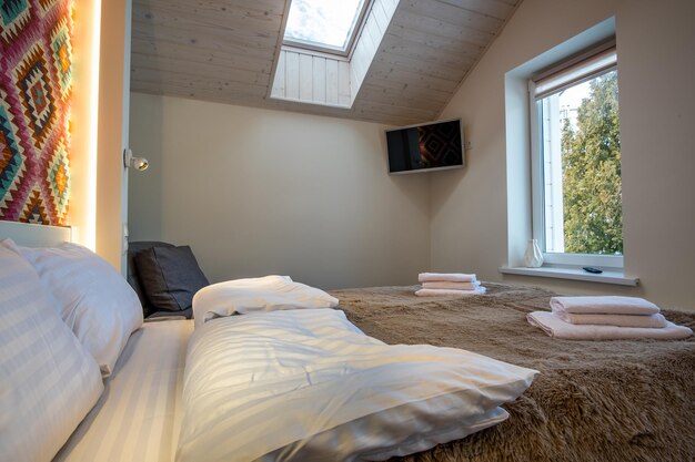 Photo interior of a spacious hotel bedroom on attic floor with fresh linen on a big double bed cozy contemporary mansard room in a modern house