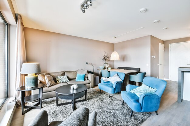 モダンなアパートのテーブルの周りのカーペットの上に置かれたクッション付きの快適なソファとアームチェアを備えたスタイリッシュなリビングルームのインテリア