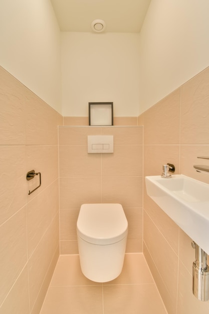 The interior of the toilet with a hinged toilet and a ceramic sink on a background of fleshcolored tiles