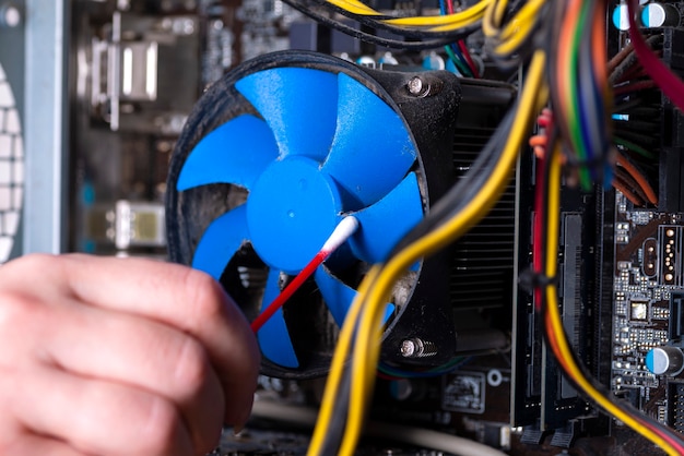 Internal parts of an old personal computer. Dusty motherboard, video card and fan. The master cleans the PC cooler from dust. Broken PC.