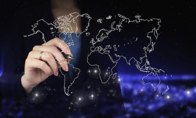 International business concept. Hand holding digital graphic pen and drawing digital hologram world, earth, map, globe sign on city dark blurred background. Navigation concept. Map and innovation