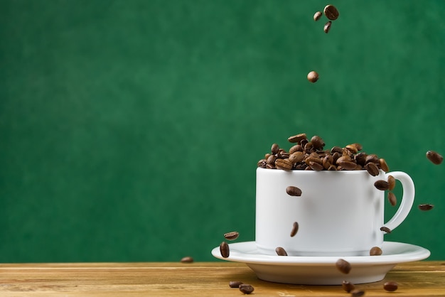 コーヒーのコンセプトの国際デー。コーヒー豆でいっぱいのクローズアップの白いコーヒーカップ。コーヒー豆は白いマグカップに落ちる