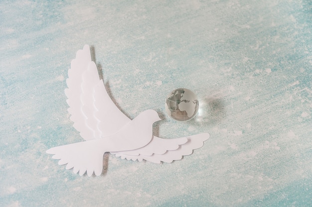 Photo international day of peace concept: white dove flying on pastel with glass globe.