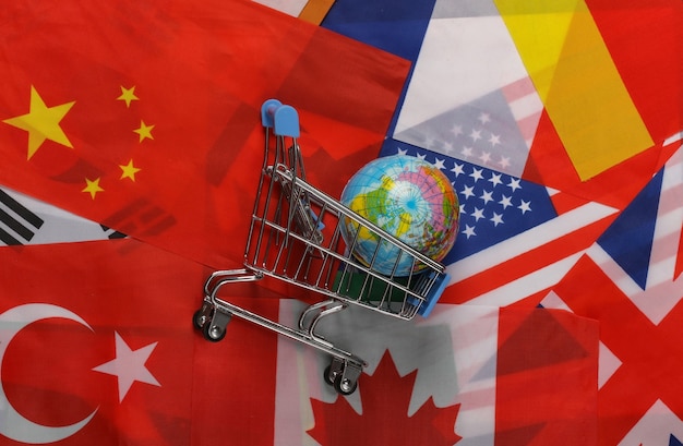 International shopping. Supermarket trolley with globe on the background of many flags of the countries