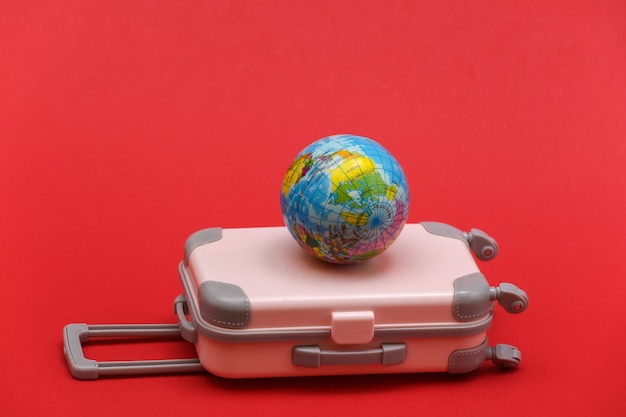 International travel concept. Mini plastic travel suitcase on red background.