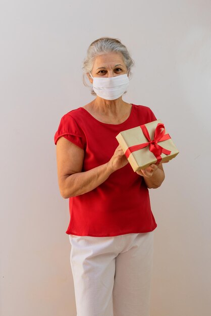 International Womens Day  Mature Woman with pandemic mask holding a gift isolated on white