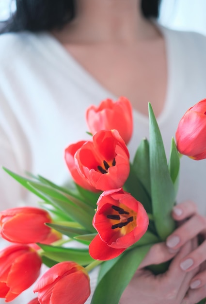 Giornata internazionale della donna primo piano di una donna con un maglione bianco e un bouquet di tulipani rossi