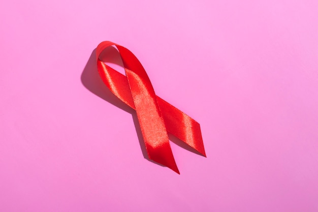 Internationale aidsdag. Rood lint met een harde schaduw op een roze achtergrond. AIDS bewustzijn concept. 1 december.